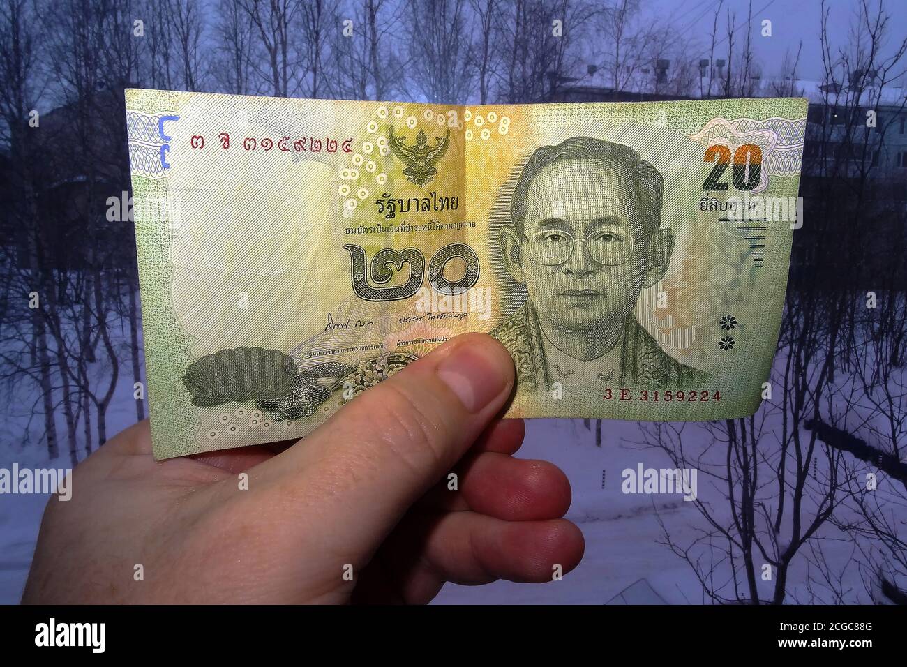 In der Hand von 20 thailändischen Baht vor dem Hintergrund einer dunklen Stadt in Sibirien. Blick von vorne. Stockfoto