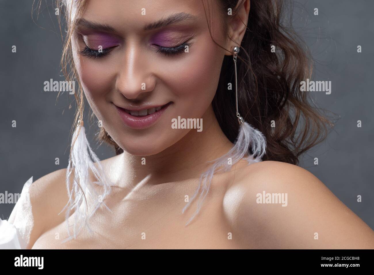 Stilvolle und elegante Braut in einem modernen Anzug, Porträt. Make-up in rosa Farbtönen, Ohrhänger mit weißen Federn. Stockfoto