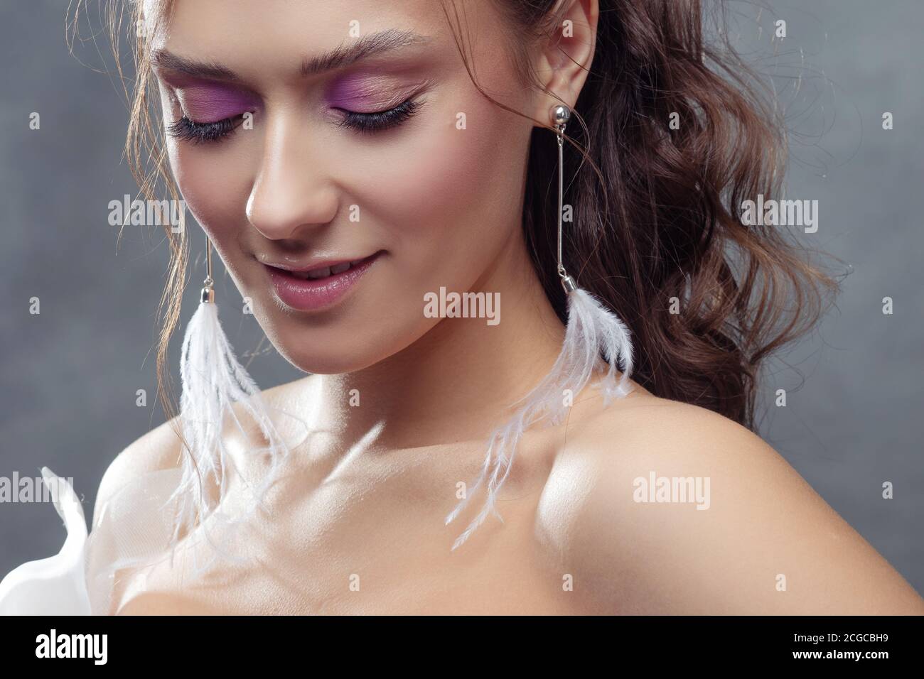 Stilvolle und elegante Braut in einem modernen Anzug, Porträt. Make-up in rosa Farbtönen, Ohrhänger mit weißen Federn. Stockfoto