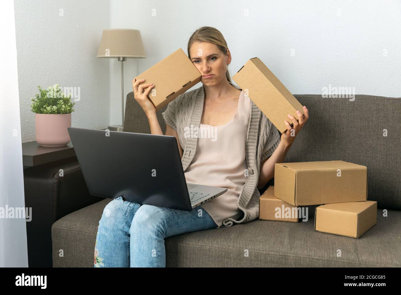 Erschöpft müde Frau kleines Handwerk Unternehmer sitzen auf Couch mit Boxen und Laptop. Verarbeitet und bereitet Sendungen aus dem Online-Shop Stockfoto