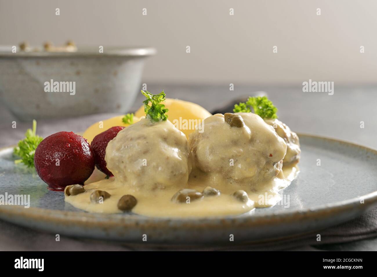 Gekochte Fleischbällchen in weißer Soße mit Kapern, in Deutschland Königsberger Klopse genannt, traditionelles Gericht mit Rote Beete Kartoffeln und Petersilie garnieren auf einem Stockfoto