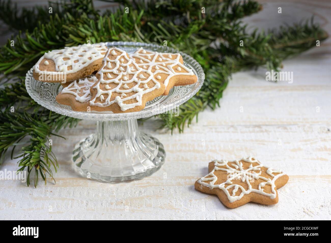 Lebkuchen Weihnachtsplätzchen auf einer festlichen Glasschale mit Tannenzweig Dekoration auf einem weiß bemalten Holztisch, Kopierraum, ausgewählter Fokus Stockfoto
