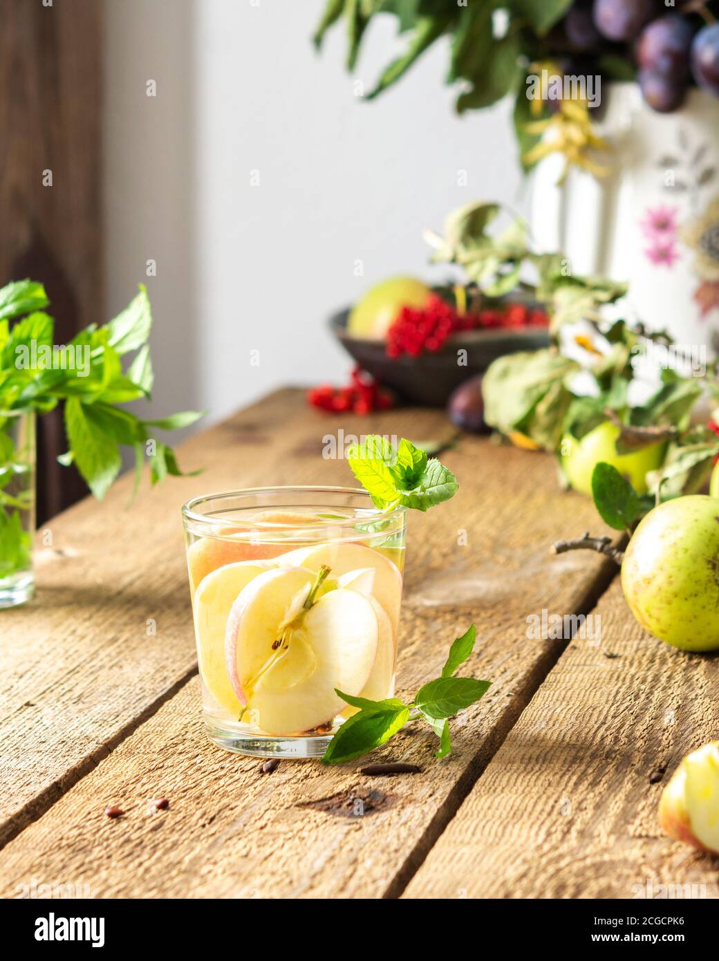 Herbst Apfelgetränk, Apfelscheiben mit Saft und Minze in einem Glas auf einem Holztisch, Blätter in einer Vase, Morgen im Dorf, rustikales Konzept Stockfoto