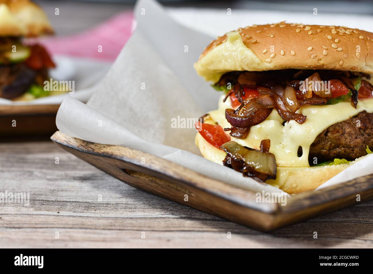 Köstlicher Gourmet-Cheeseburger mit glasierten karamellisierten roten Zwiebeln, schweizer Käse, Gurken und filettierten Tomaten Stockfoto