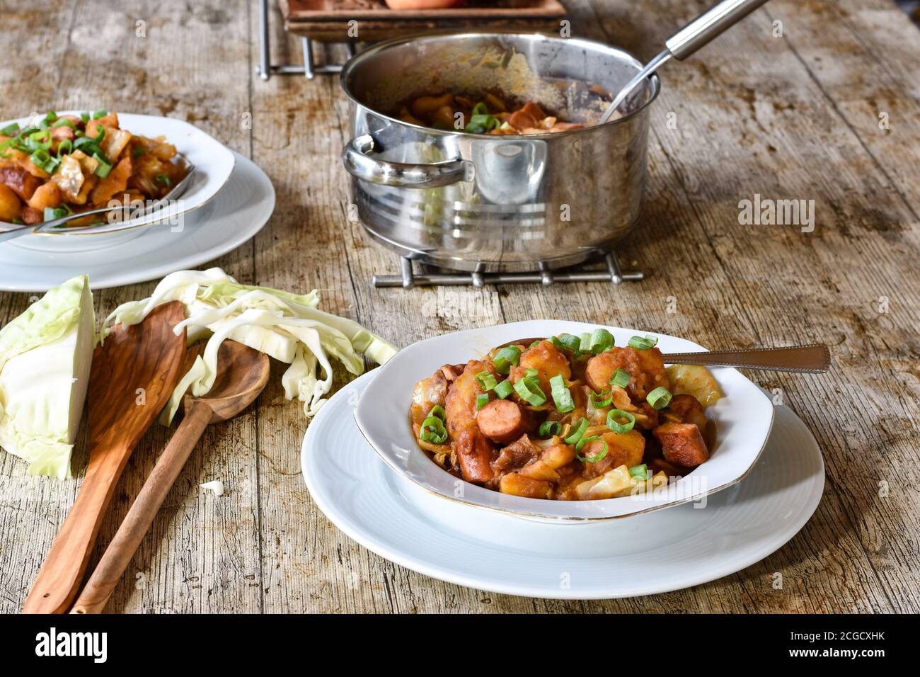 2 weiße Teller Wiener Kartoffelgulasch/Eintopf serviert Auf einem rustikalen Holztisch mit Suppentopf zum Abendessen Stockfoto