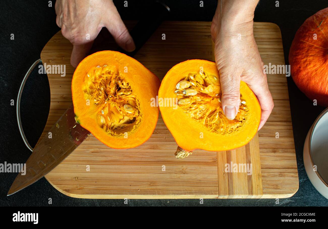 Frauenhänden schneiden gerade einen hokkaido-Pumpkin in die Hälfte Stockfoto