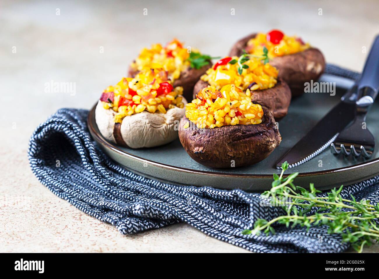 Gebackene gefüllte portobello-Pilze mit Bulgur-Pilaf und gehacktem Gemüse. Leckeres und nahrhaftes vegetarisches Gericht. Steinhintergrund. Stockfoto