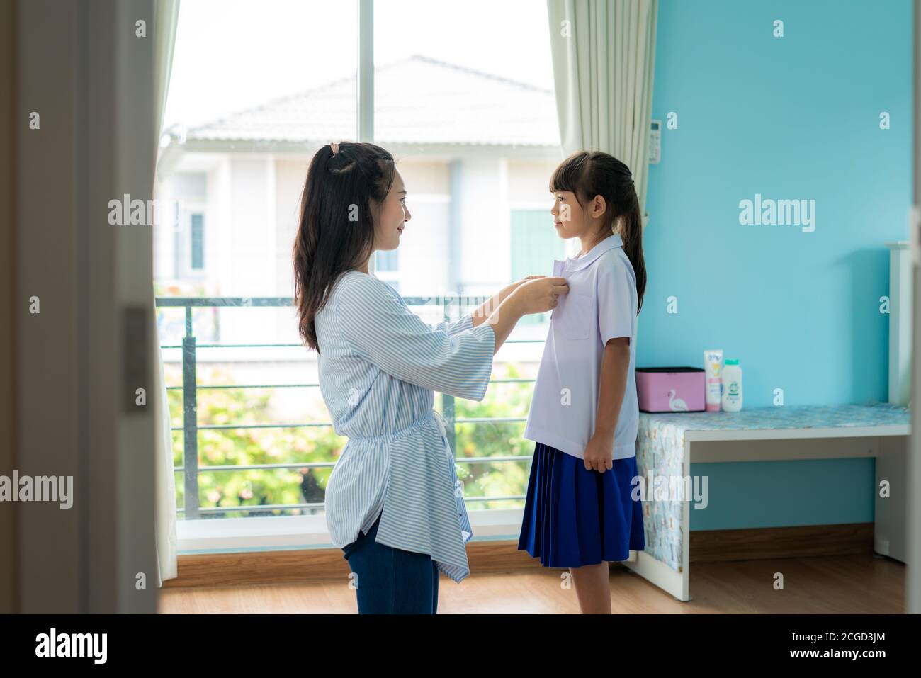 Asiatische Mutter Vorbereitung Grundschüler Uniform zu ihrem kleinen Tochter für die Schule im Wohnzimmer zu Hause. Die morgendliche Schulroutine für den Tag in der LIF Stockfoto