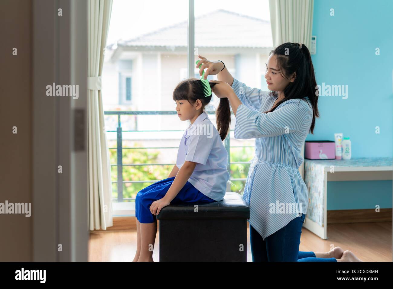 Asiatische Mutter kämmt die Haare ihrer Tochter am Morgen, bevor sie zur Schule im Wohnzimmer zu Hause gehen. Die morgendliche Schulroutine für den Tag im li Stockfoto
