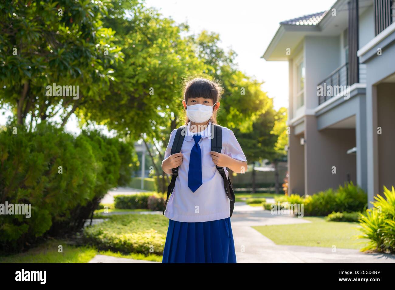 Porträt von niedlichen asiatischen Grundschule Mädchen in medizinische Maske vor zu Hause während COVID-19 Pandemie. Die morgendliche Schulroutine für den Tag im Leben g Stockfoto