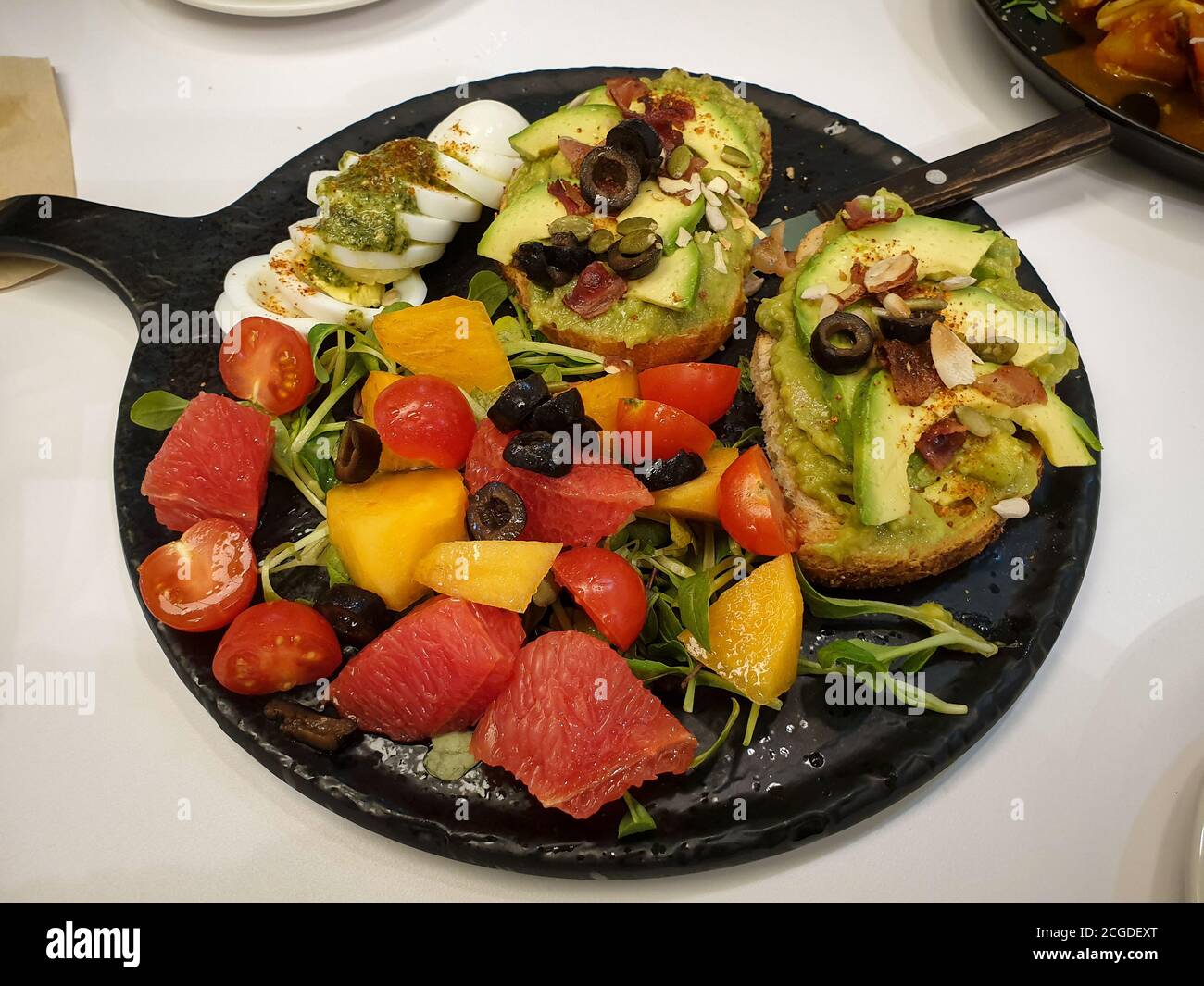 Baguette mit in Scheiben geschnittenen Avocado, Guacamole, Oliven, und Mandeln und anderen Nüssen gekrönt. Stücke von frischen Früchten. Kirschtomate, Grapefruit und Kaki. Stockfoto