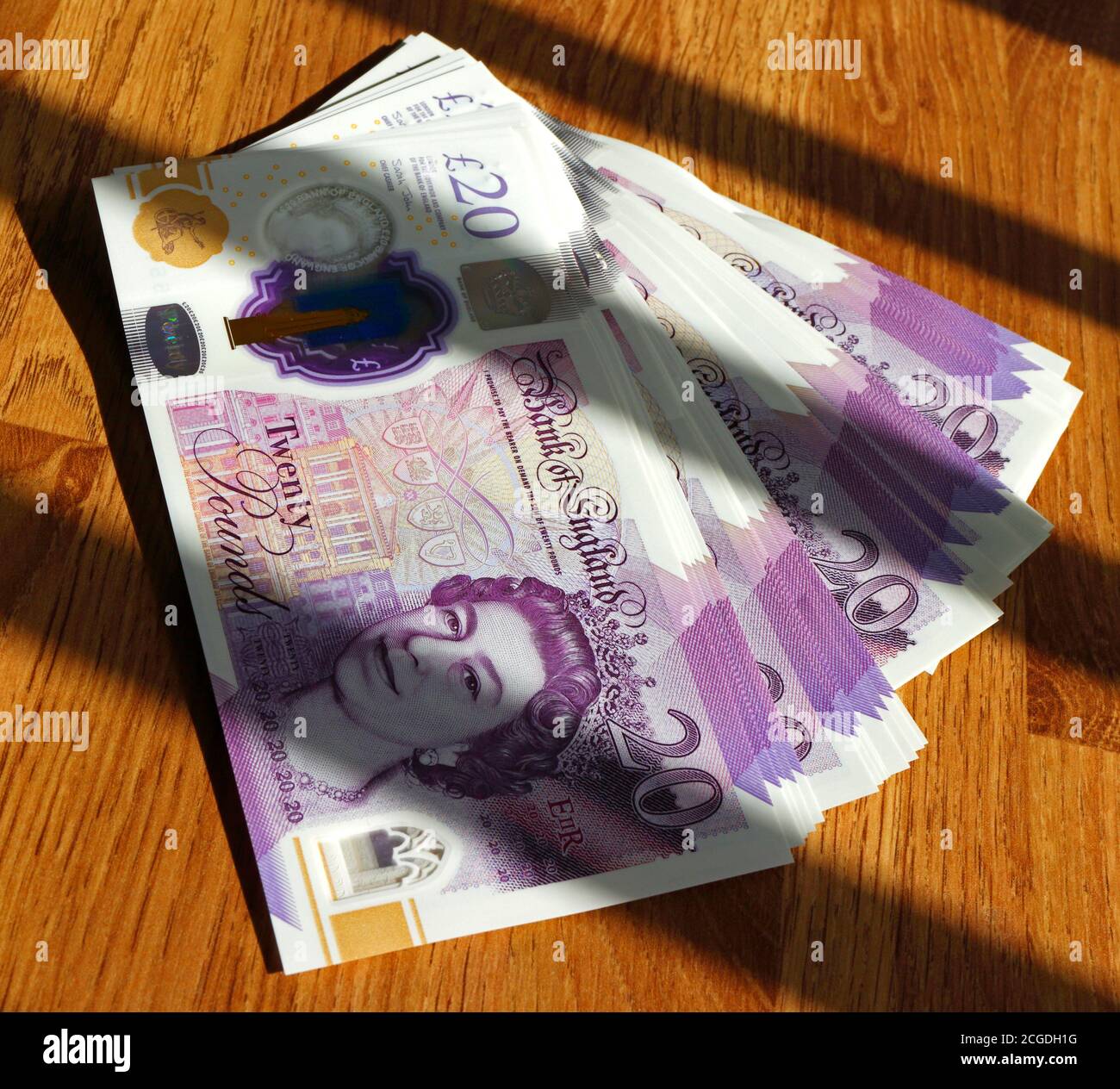 Ein gebräunter Haufen von zwanzig Pfund Noten auf einem Tisch in Sonnenschein mit diagonalen Schatten. Stockfoto