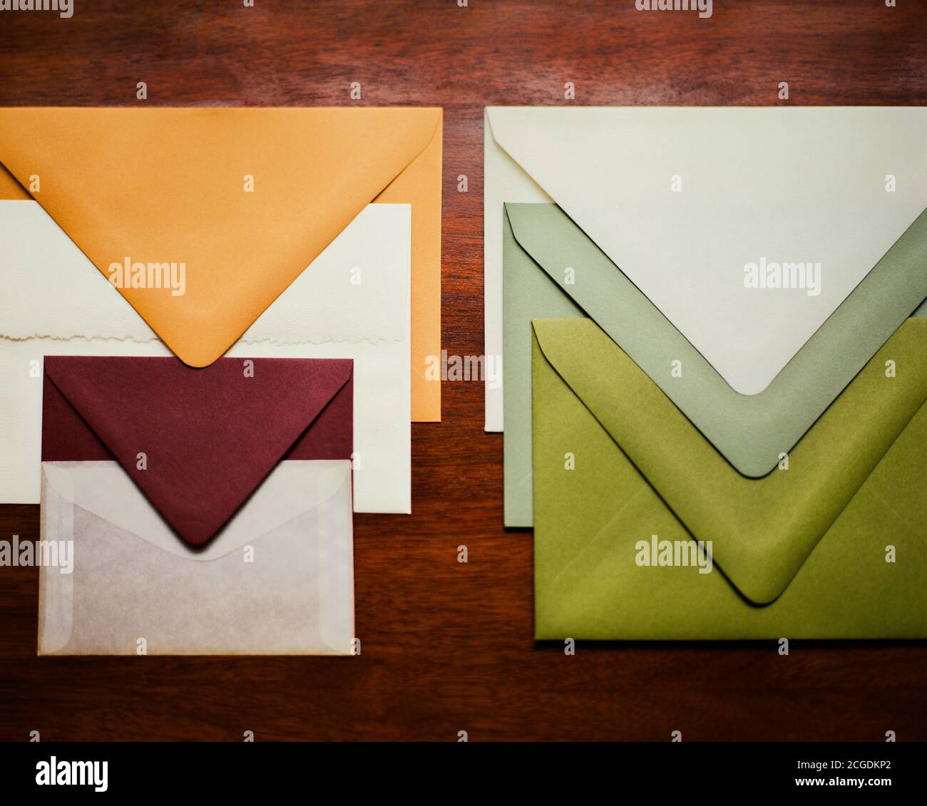Bunte grüne, cremefarbene, kastanienbraune Briefumschläge auf Holz gestapelt Stockfoto