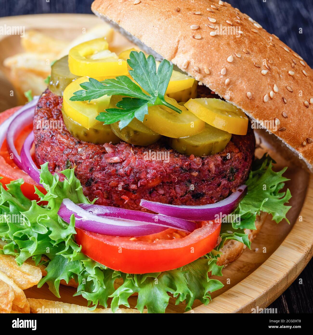 Pflanzenbasierter veganer Rübenburger mit Gurken frischer Salat, Tomaten, rote Zwiebeln im Brötchen mit Sesamsamen darauf, französische Braten, Ketchup auf Bambus Stockfoto