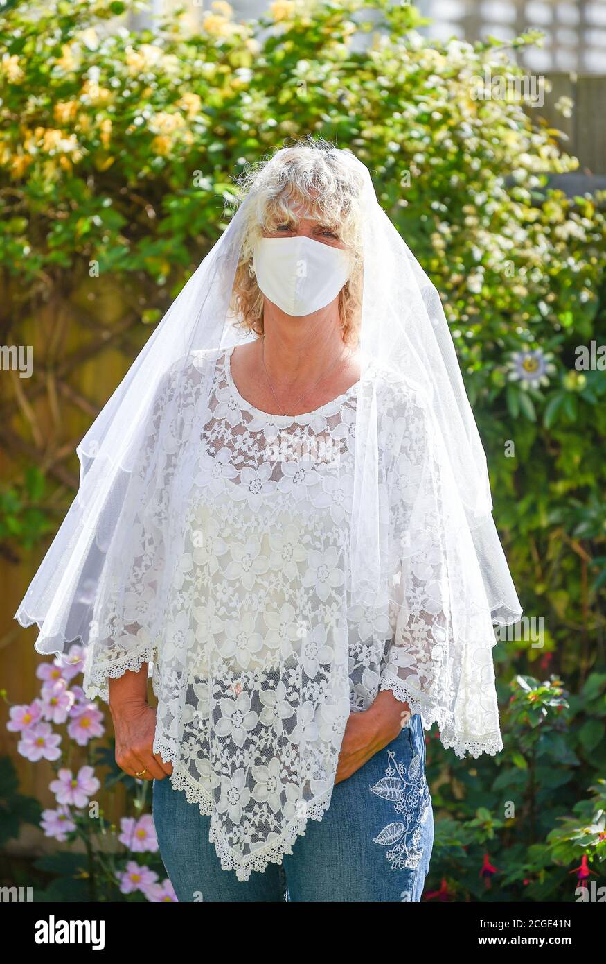 Reife Frau weiblich trägt ihre alte Hochzeit Schleier und ein Gesichtsmaske während der Coronavirus COVID-19 Pandemie Stockfoto