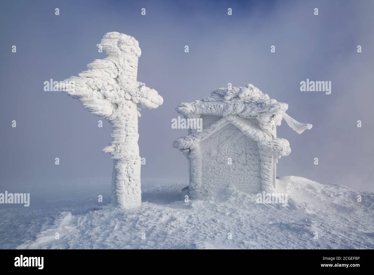 Schnee coted Gebäude und Kreuz auf einem schneebedeckten Rasen. Nebel auf dem Hintergrund. Fantastische Winterlandschaft. Stockfoto