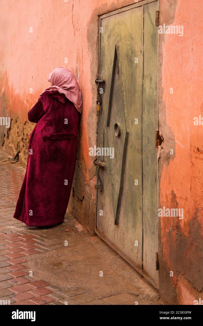 Eine marokkanische Frau in traditioneller Kleidung lehnt sich an eine verwitterte Wand im Souk von Marrakesch, Marokko Stockfoto