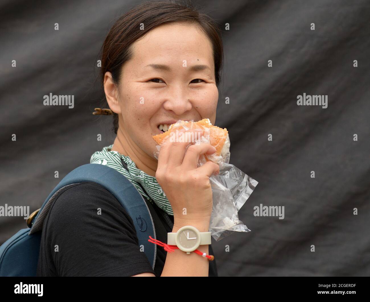 Weibliche japanische Tourist isst ein Brötchen und lächelt für die Kamera. Stockfoto