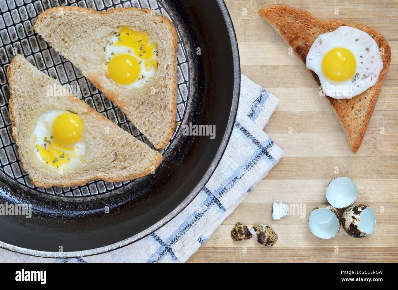 Gebratene Brotscheiben mit Wachteleiern auf einer Bratpfanne auf einem hölzernen Schneidebrett mit Küchentuch und Eierschalen, Draufsicht. Gesunde Ernährung. Stockfoto