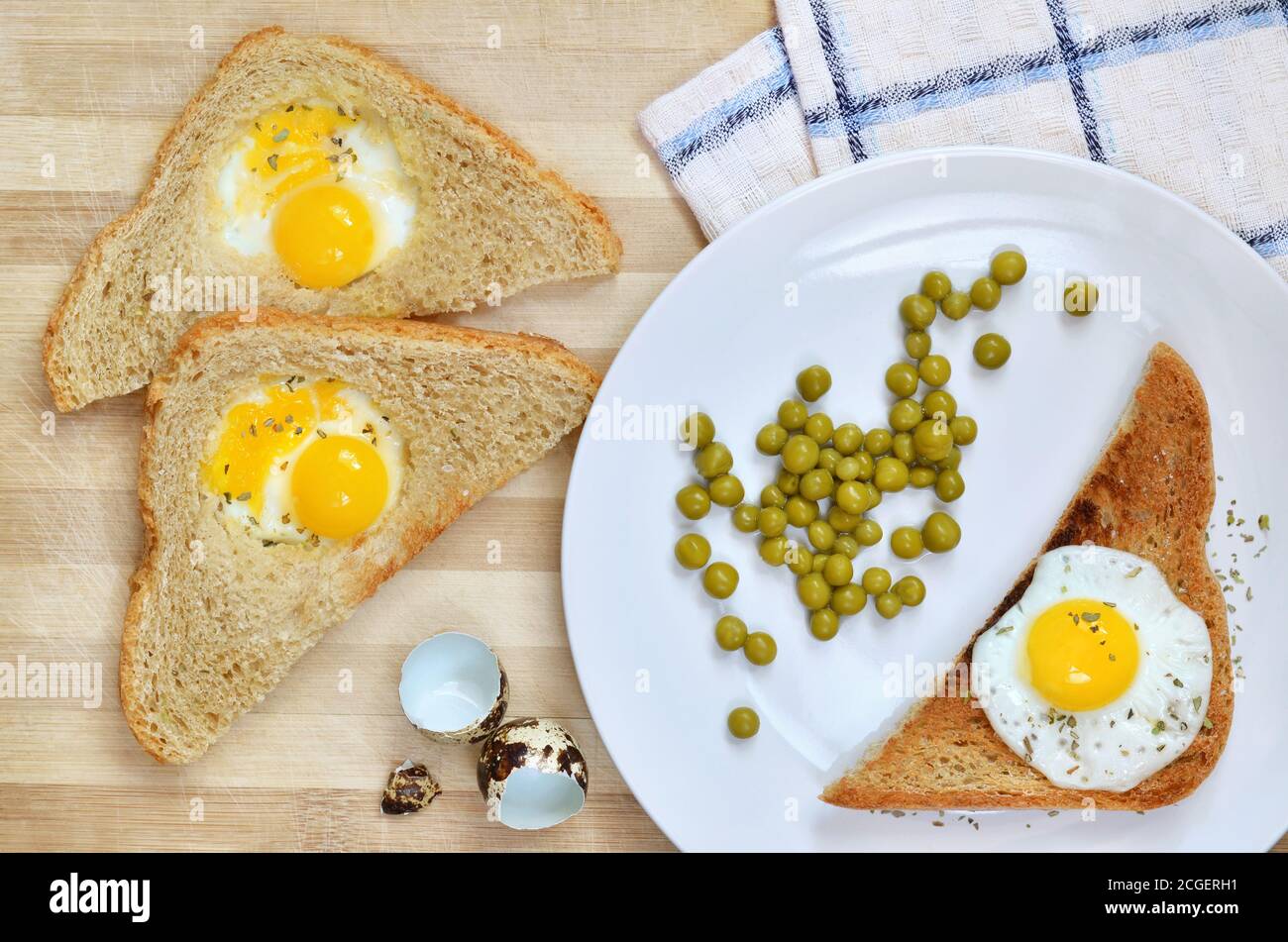 Toast mit gebratenen Wachteleiern und grüner Erbse auf einem weißen Teller auf einem Holzschneidebrett, Draufsicht. Gesunde Ernährung. Stockfoto