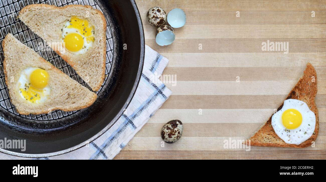 Gebratene Brotscheiben mit Wachteleiern auf einer Bratpfanne, die auf einem hölzernen Schneidebrett als Hintergrund platziert ist, mit Küchentuch und Eierschalen, Draufsicht Stockfoto
