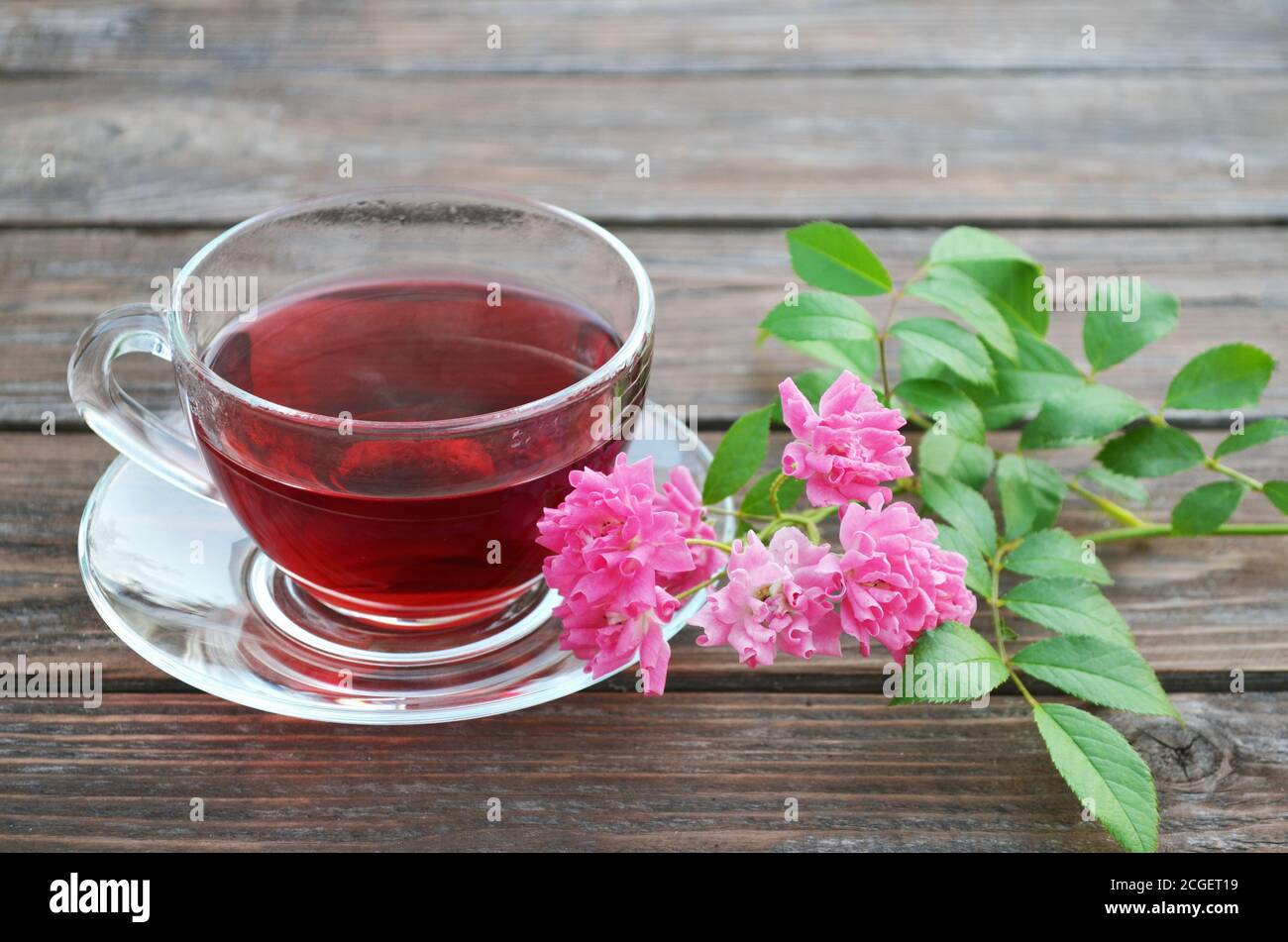 Tasse frisch zubereiteter heißer Tee und rosa Rosen auf einem alten Holztisch. Stockfoto
