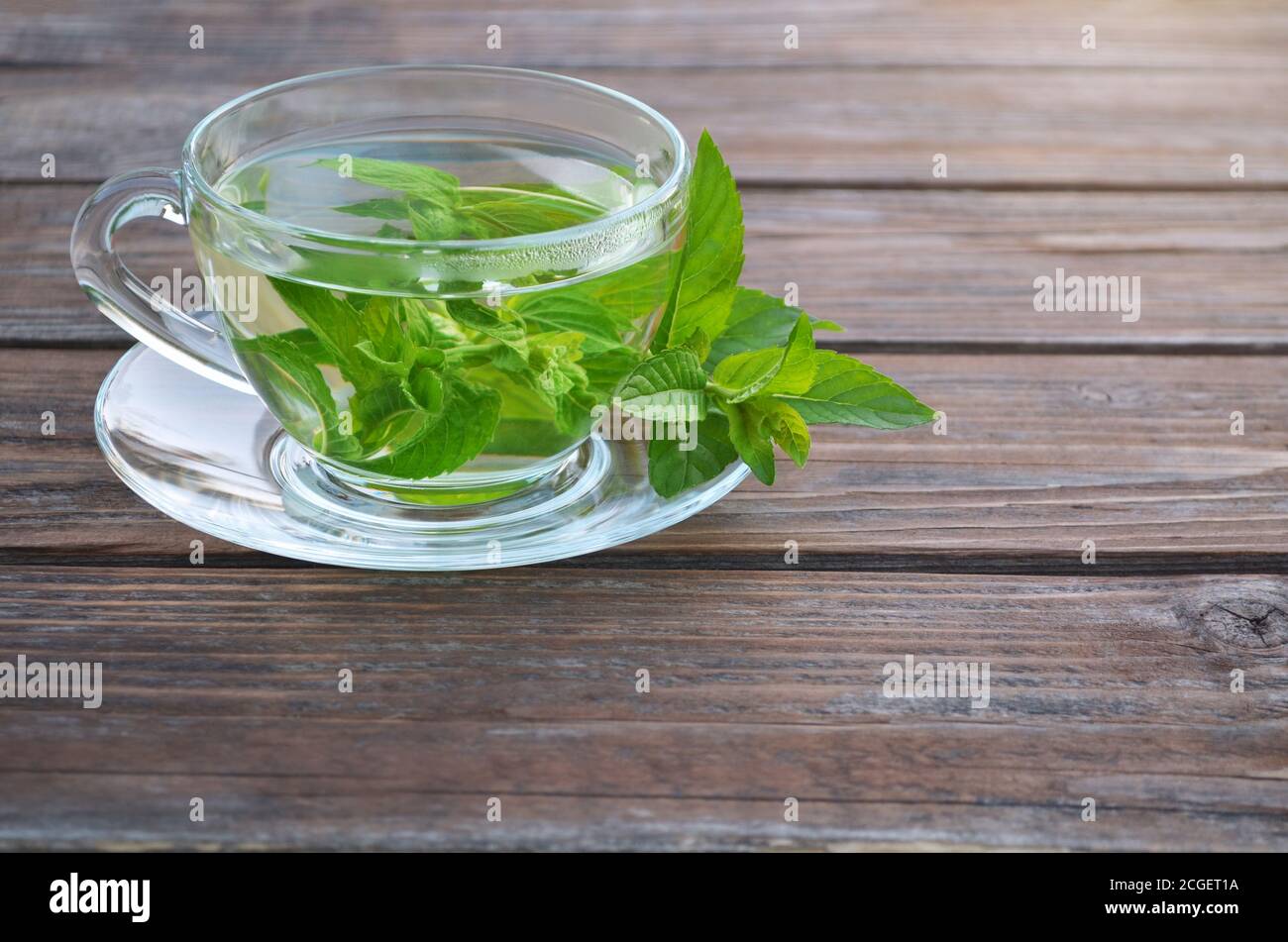 Frisch zubereiteter, aromatischer Minztee in einer Glasschale und frische Blätter auf einem Holztisch aus nächster Nähe. Konzept eines gesunden Lebensstils. Stockfoto