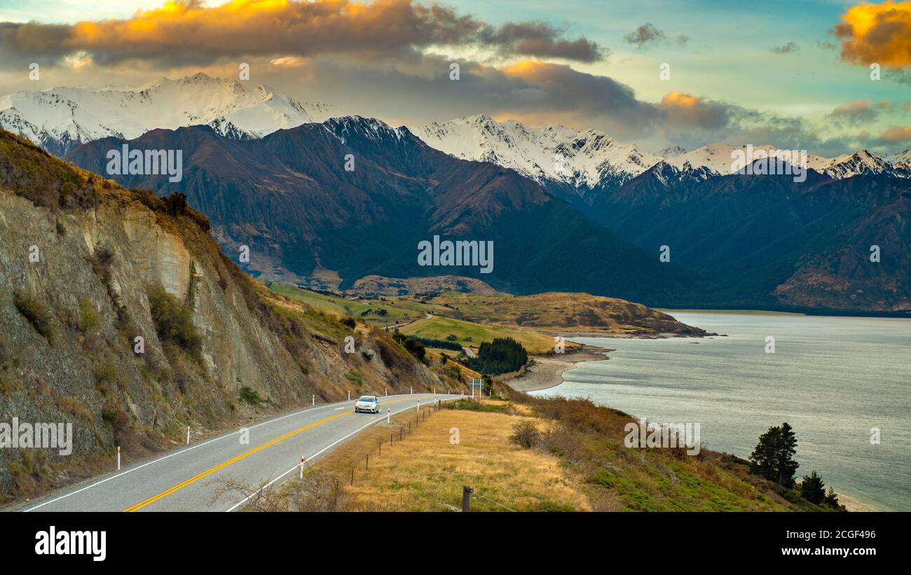 Ein Auto lief auf einer Straße am Seeufer. Der Hintergrund ist ein toller Berg am Abend. Schöne Wolken am Hawea See Aussichtspunkt in Wanaka Ota Stockfoto