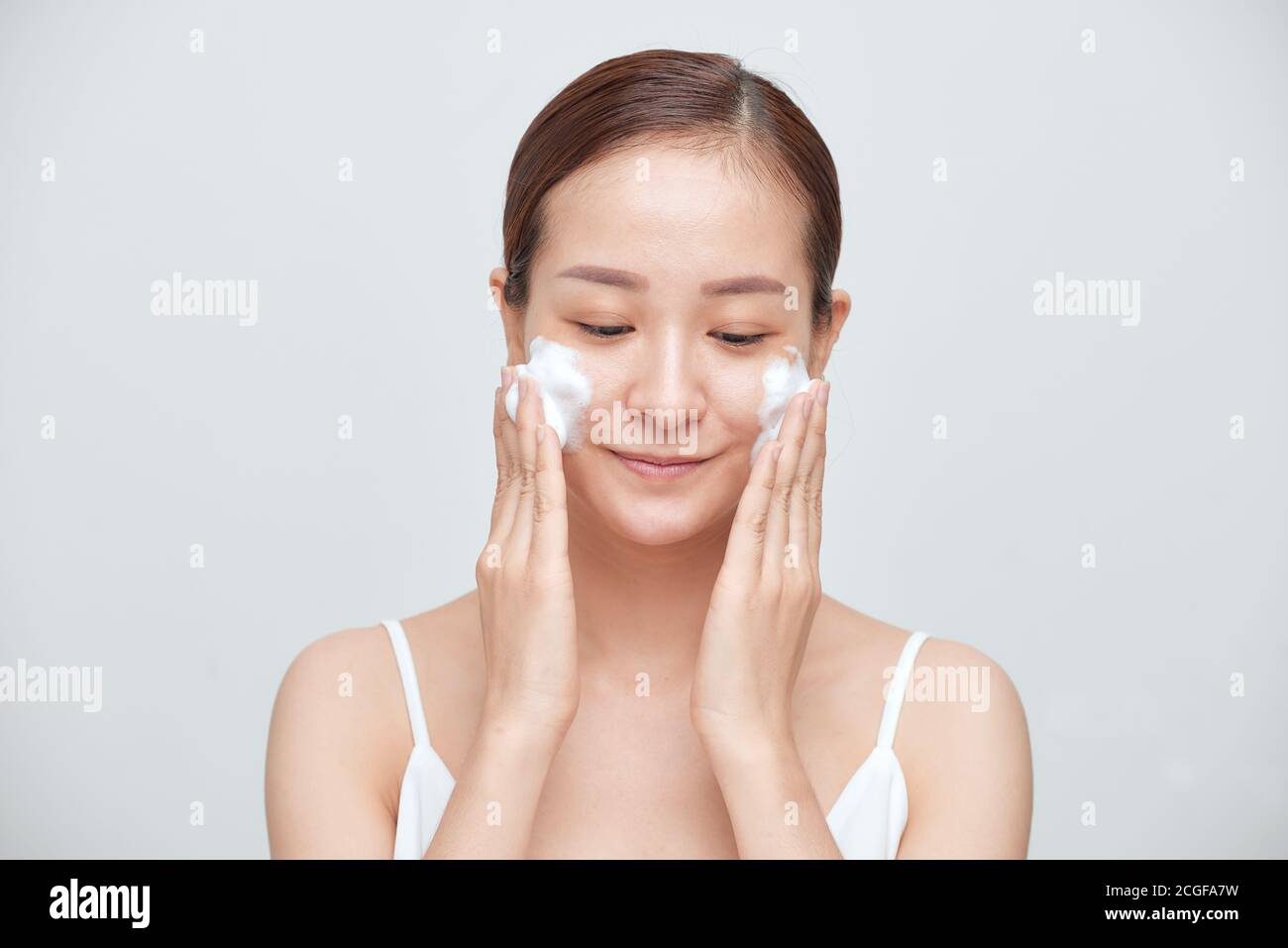 Porträt der jungen asiatischen Frau, die schäumende Reinigungsmittel auf weißem Hintergrund auflegt. Stockfoto