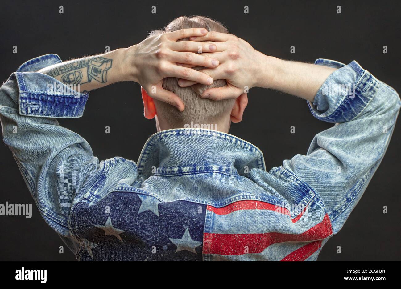 Rückansicht des jungen Mannes, der Denim-Jacke mit usa-Flagge trägt, posiert im Studio mit erhobenen Händen. Herrenbekleidung, Bekleidung Mode. Isoliert über Schwarz Stockfoto