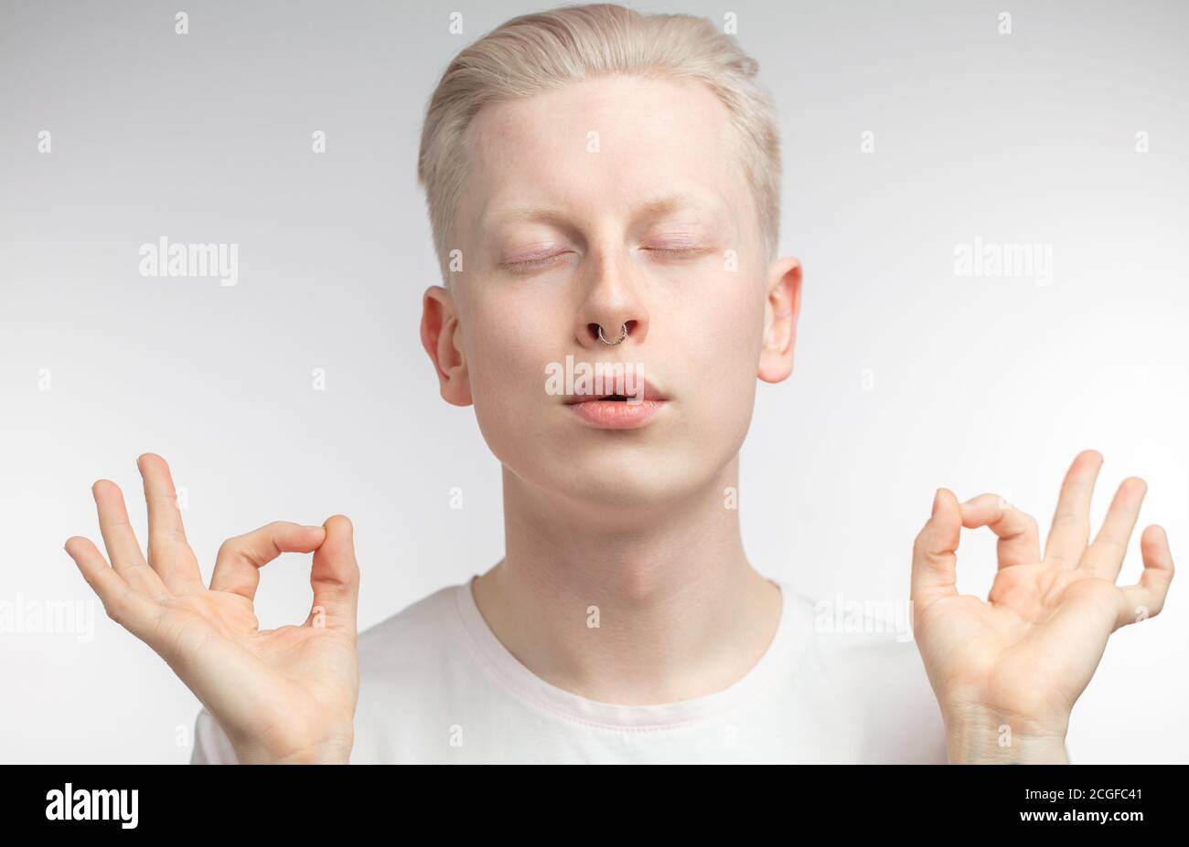 Heiterer Albino Mann hält Finger in Mudra, mit geschlossenen Augen, üben Gruppenmeditation im Studio versucht zu entspannen, Posen vor weißem Hintergrund. Pe Stockfoto