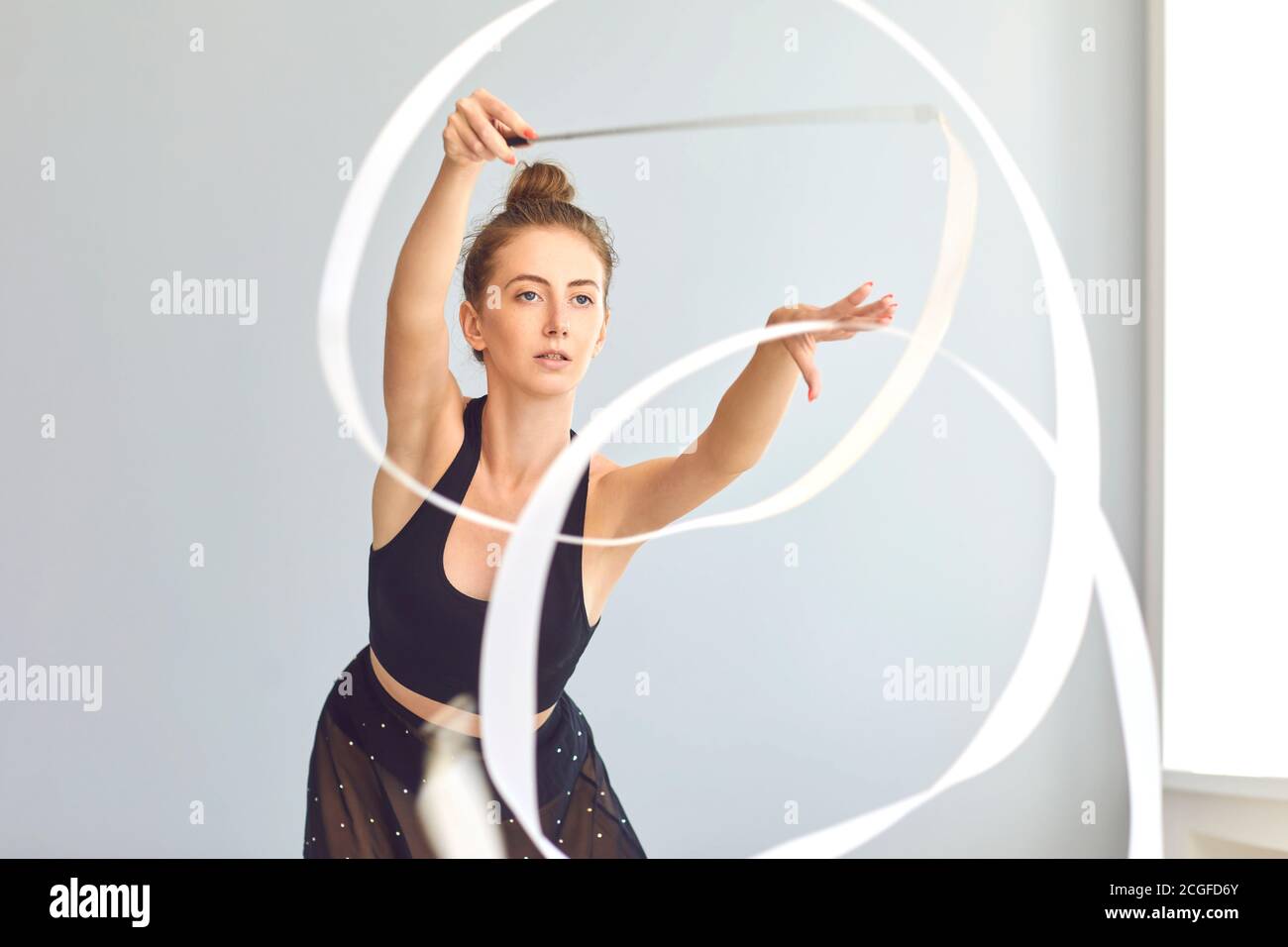 Gut aussehende junge weibliche rhythmische Turnerin Proben Element mit Band Im modernen Fitnessraum Stockfoto