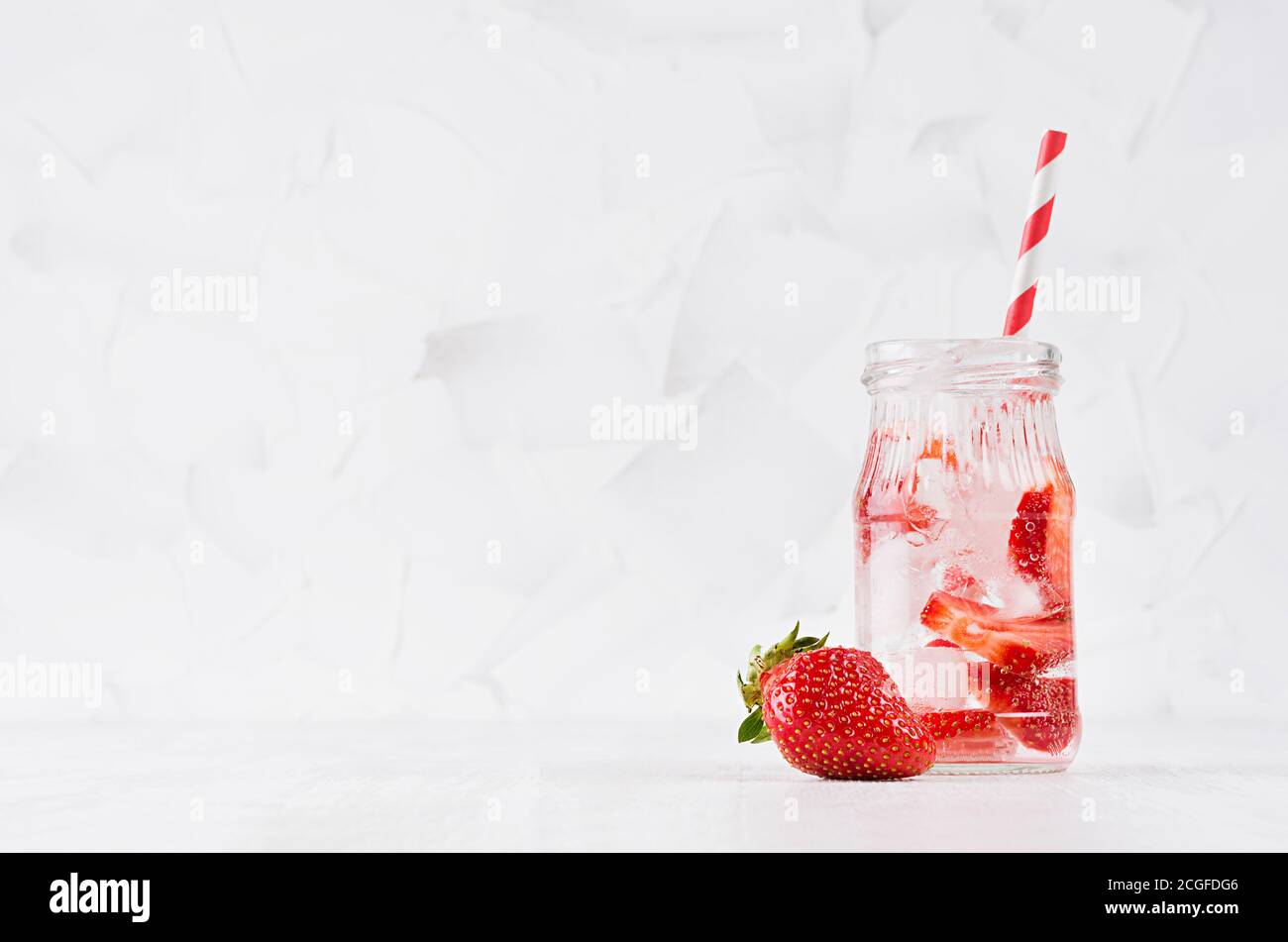 Natürlicher Bio-Cocktail mit Erdbeere, kohlensäurehaltiges Wasser und Eiswürfeln mit gestreiftem Stroh auf hellweißem Holzbrett und Wand, Kopierraum. Stockfoto