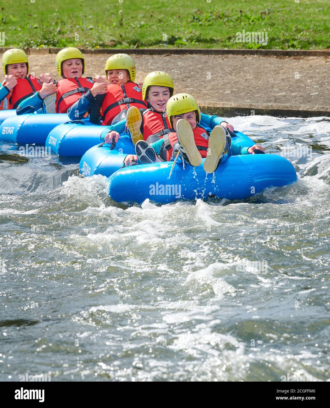 Eine Gruppe von Teenagern, in einzelnen Gummiringen, zusammengeschlossen, steigt den künstlichen Wildwasserkurs in Northampton, England. Stockfoto