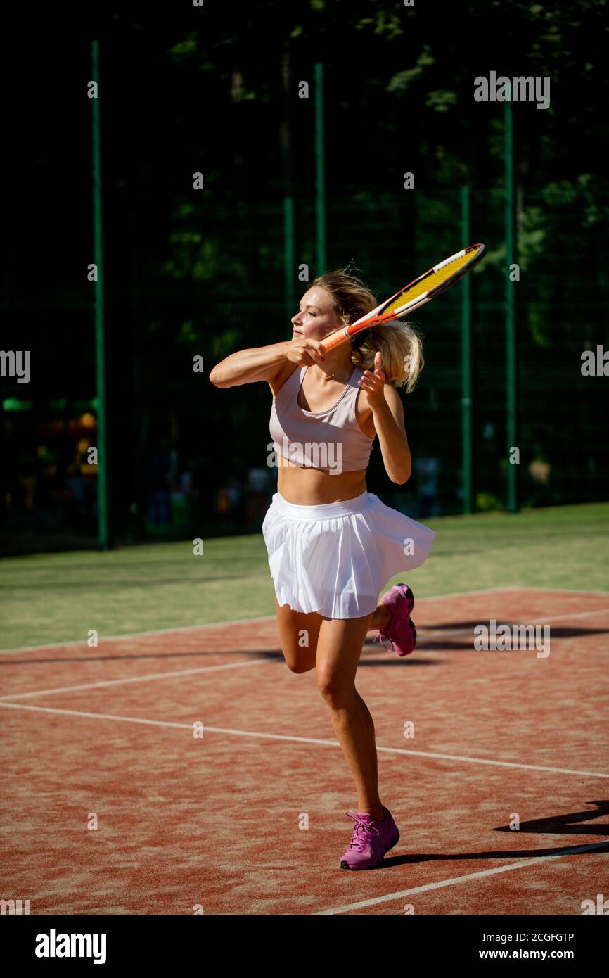Tennis spielen sportliche Frau schlagen Kugel auf roten Hartplatz.  Kaukasische Athlet Mädchen wieder mit Schläger tragen weiße Rock und rosa  Schuhe Stockfotografie - Alamy