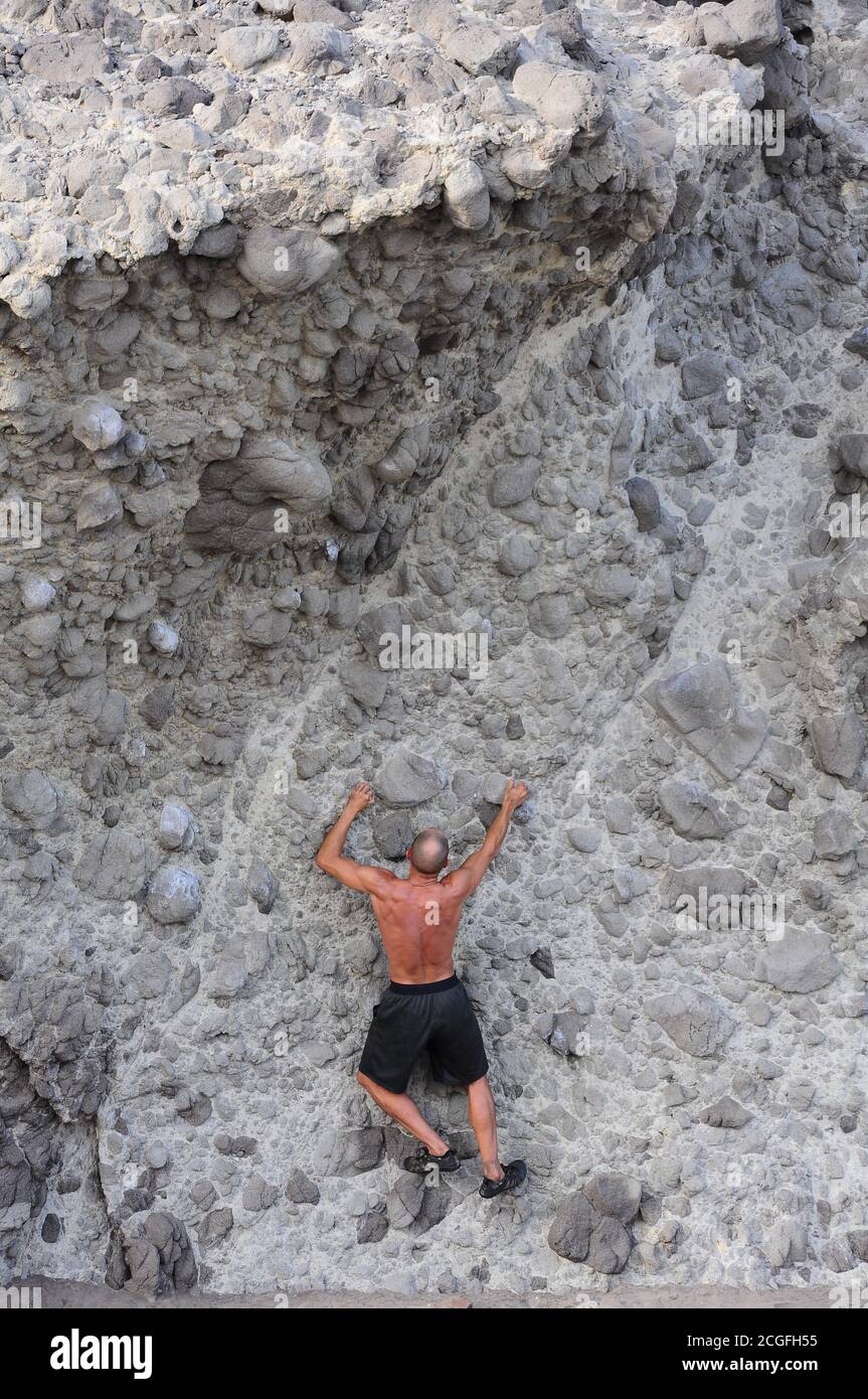 Mann übt Alpinismus, während er eine vertikale Felswand klettert Stockfoto