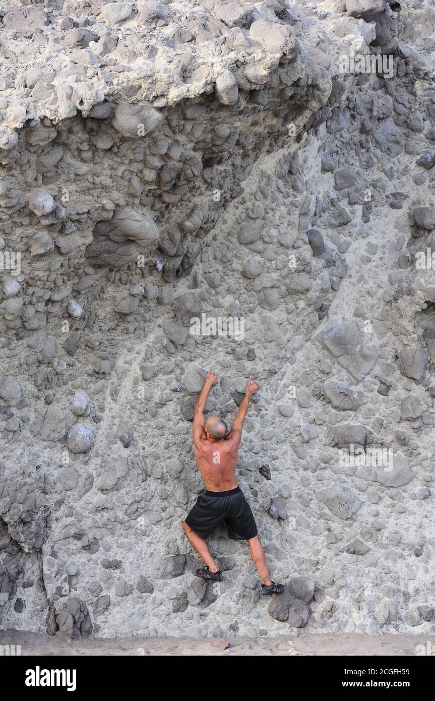 Mann, der eine vertikale, vulkanische Felswand klettert Stockfoto