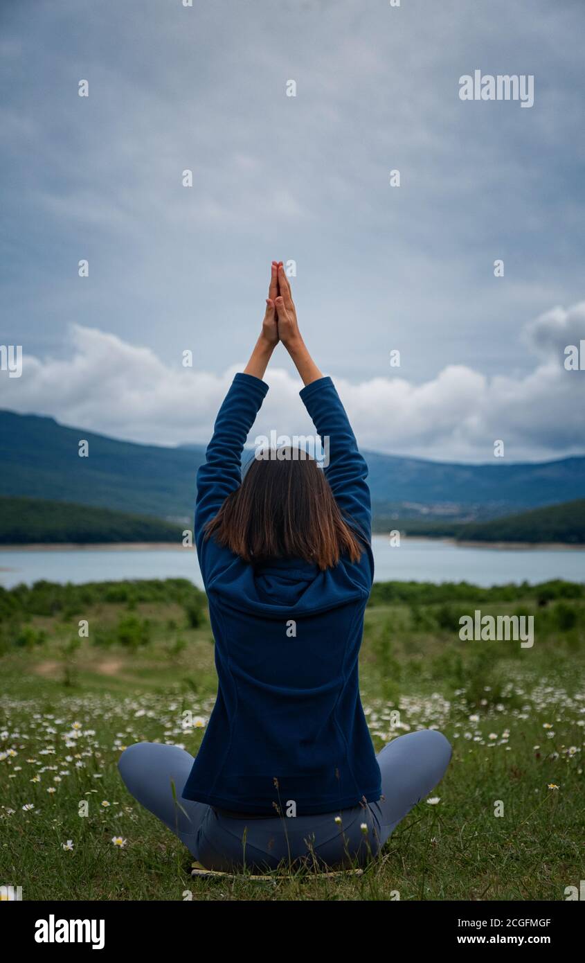 Eine junge Frau, die Yoga auf dem Feld macht. Sensibilität für die Natur. Selbstanalyse und Seelenforschung. Spirituelles und emotionales Konzept. Rückansicht Stockfoto