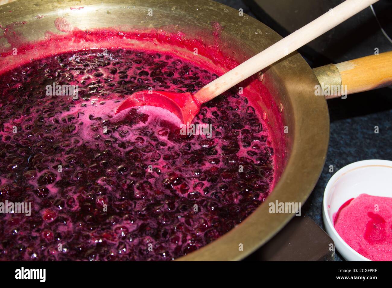 Zu Hause wird schwarze Johannisbeermarmelade in einem Kupferbecken gekocht und mit einem Holzlöffel vermischt Stockfoto