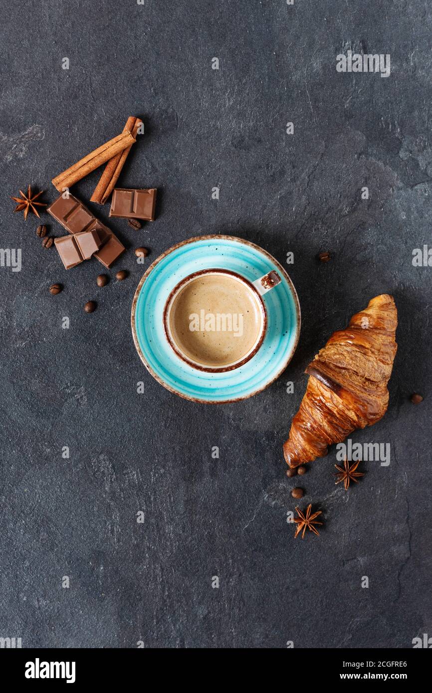 Tasse Kaffee mit Zimt und Anis-Gewürz, Schokoladenstückchen und Croissant auf schwarzem Hintergrund Draufsicht. Vertikale Ausrichtung. Stockfoto