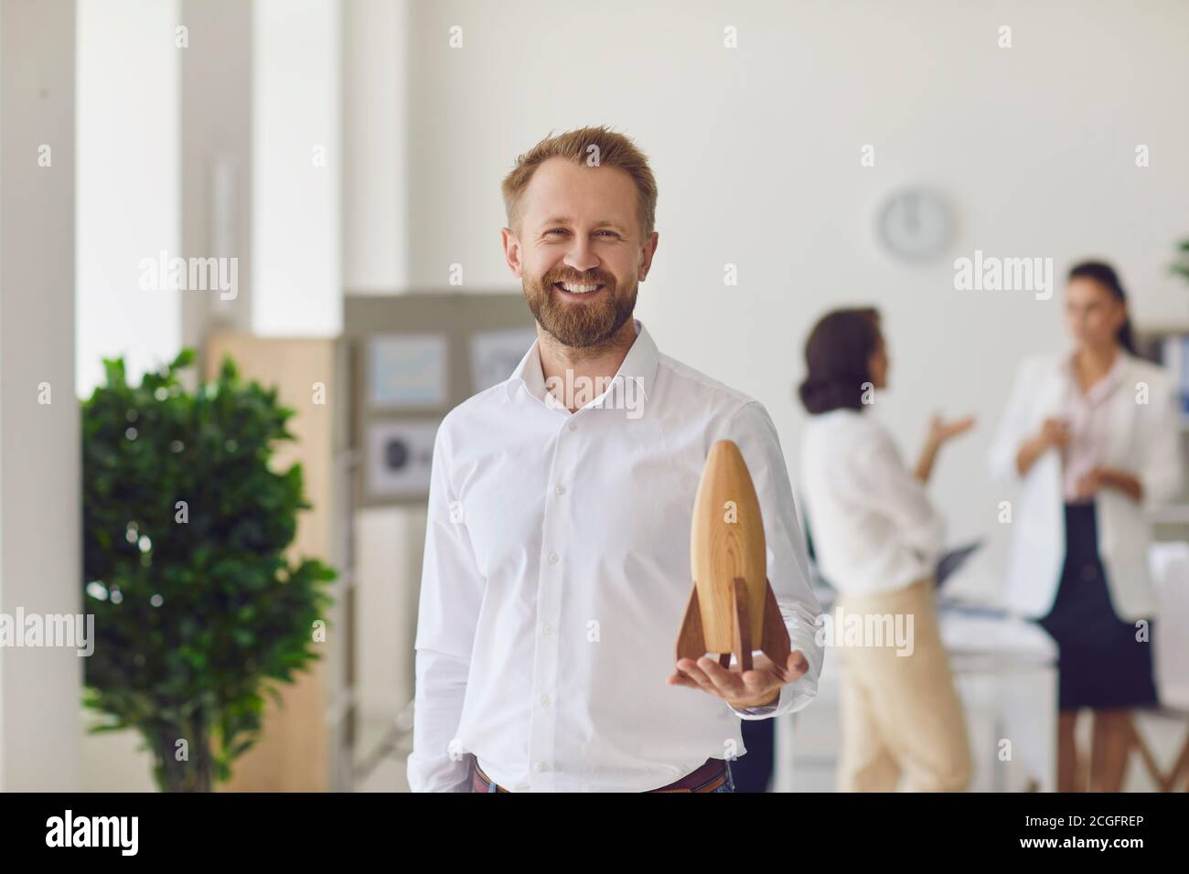 Glücklicher lächelnder Geschäftsinhaber, der die Kamera ansah und Holz hielt Rakete als Symbol des neuen Start-up Stockfoto