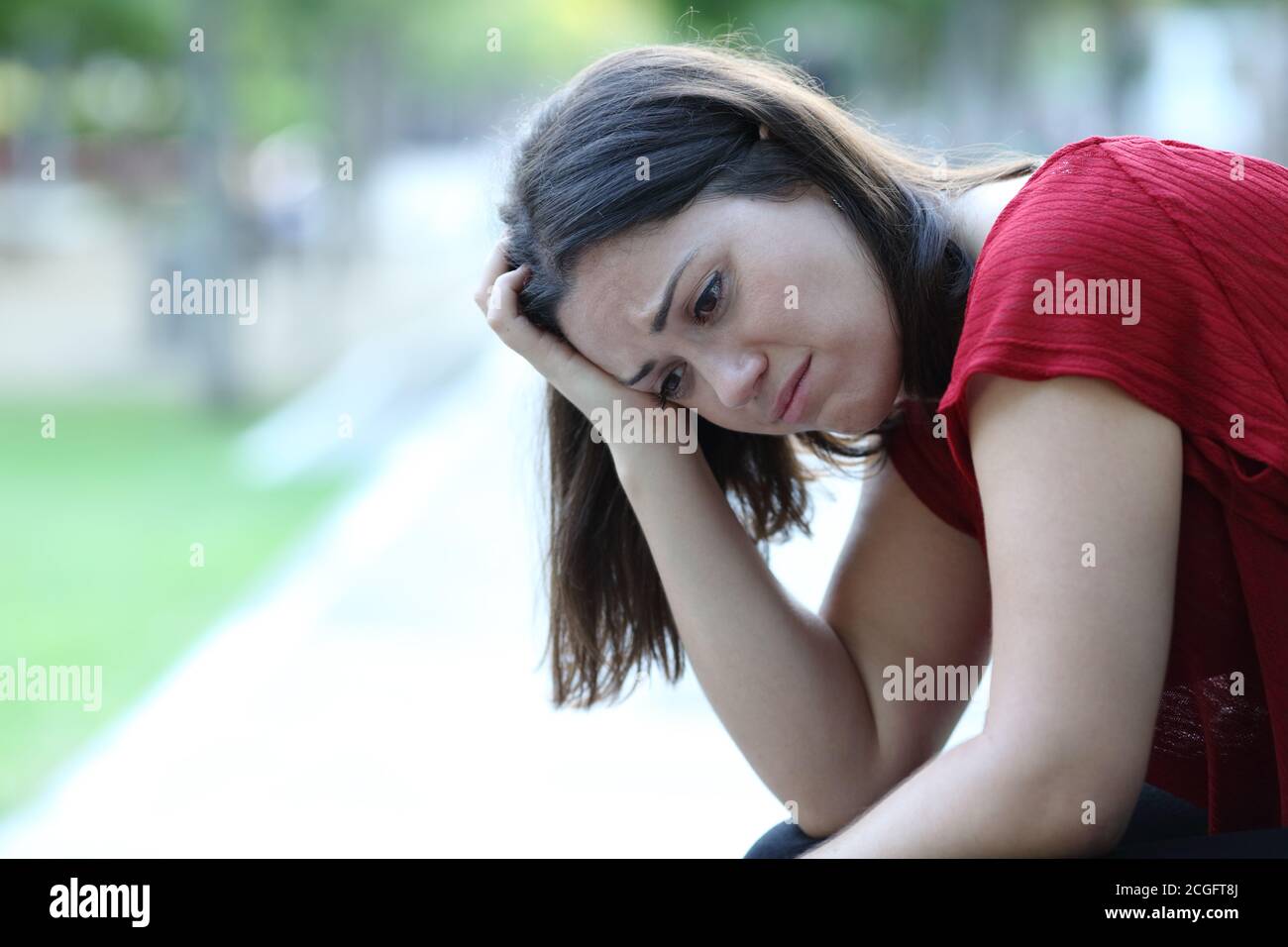 Traurige Frau, die auf einer Bank in einem Park sitzt und sich beschwert Wegschauen Stockfoto