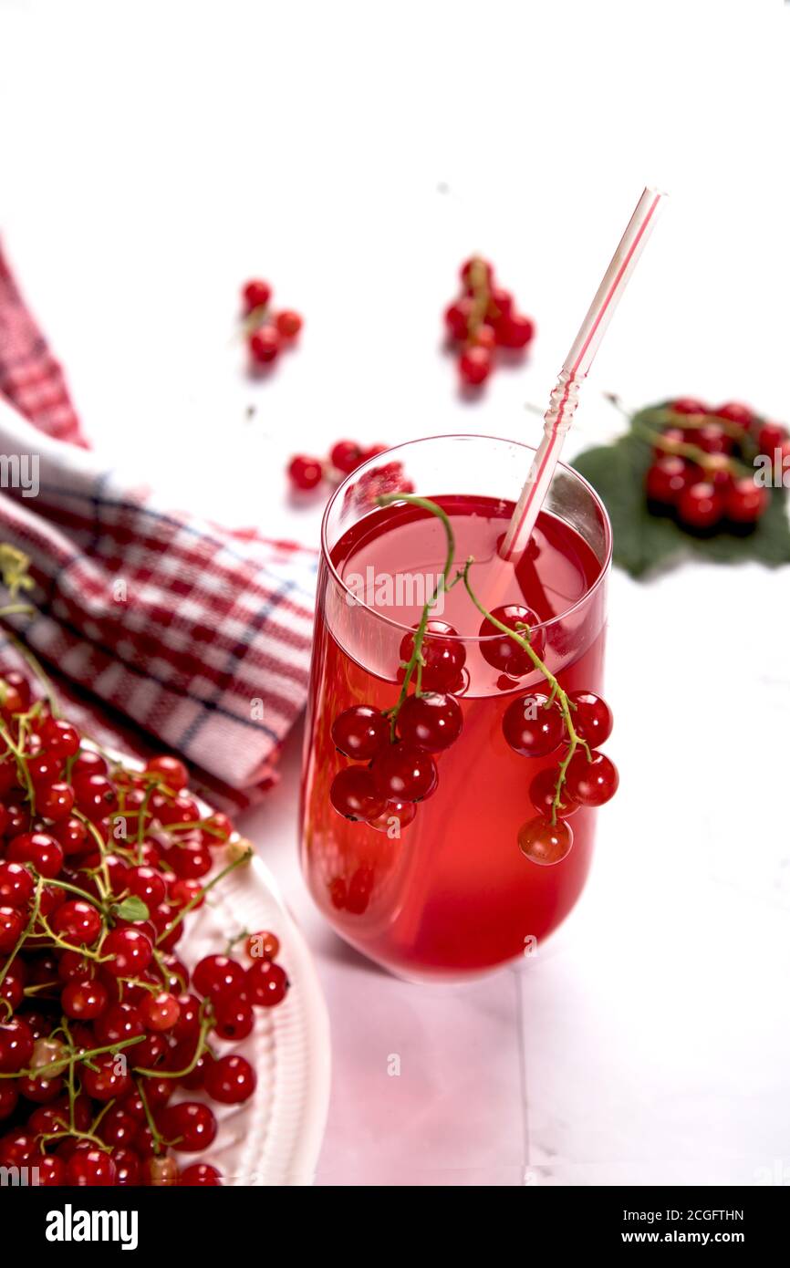 Auf einem weißen Teller liegen Zweige roter Johannisbeeren, auf hellem Hintergrund steht eine Beerenmorse in einem Glas, neben einer Serviette in rot und w Stockfoto