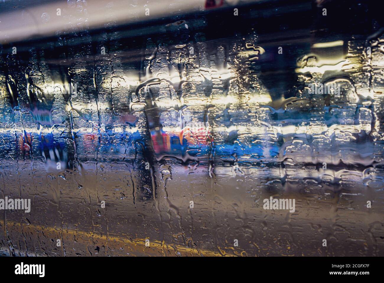 Regen auf einem Zugfenster verdunkelt den Blick auf Bahnhof, Felder und Gebäude draußen. Stockfoto