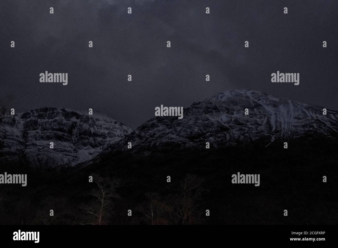 Schneebedeckte Berge in der Nacht, kaum gesehen durch den dunklen set aginsta wolkigen dunklen Himmel. Stockfoto