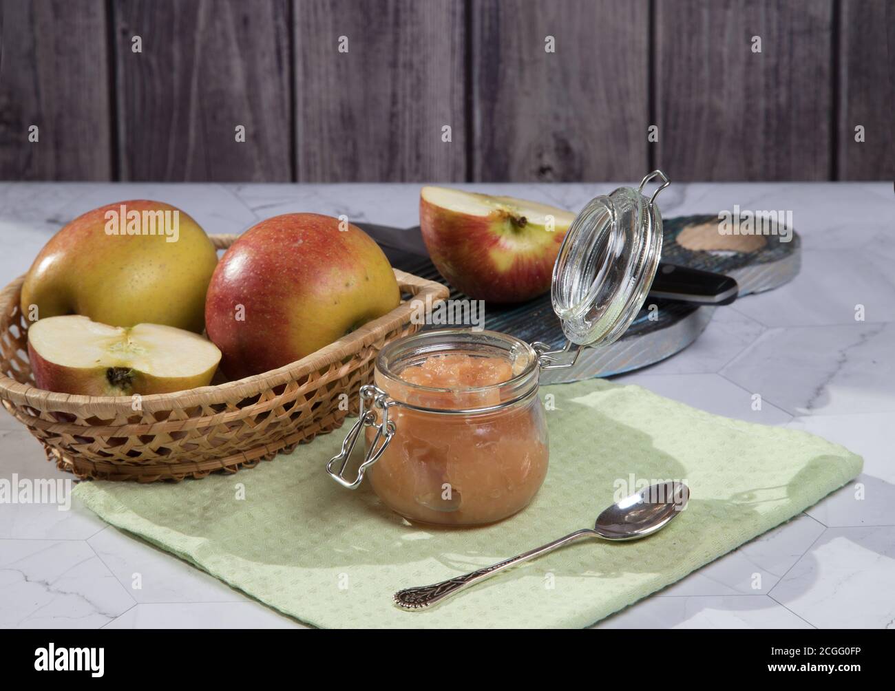 Eine Dose Apfelmus und Äpfel in einer Weidenplatte auf hellem Hintergrund, ein in Scheiben geschnittener Apfel auf einem Holzbrett. Horizontale Ausrichtung Stockfoto