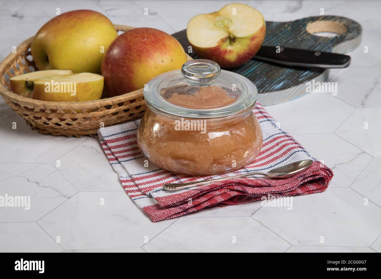 Eine Dose Apfelmus und Äpfel in einer Weidenplatte auf hellem Hintergrund, ein Apfel mit einem Messer auf einem hölzernen Schneidebretchen.Horizontale Ausrichtung Stockfoto