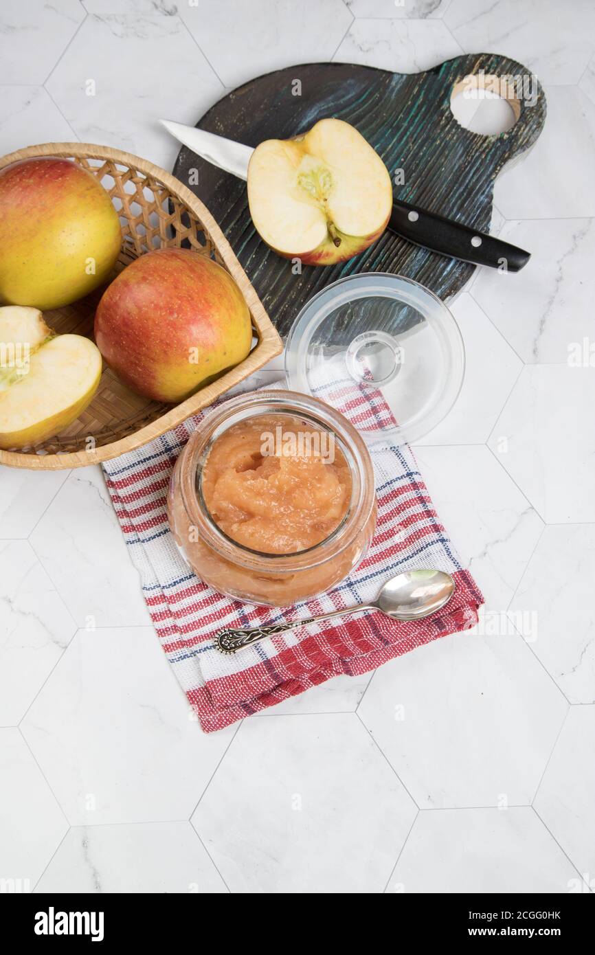 Glas mit Apfelmus und frischen Äpfeln auf einem Teller auf hellem Hintergrund mit karierter Serviette. Flach.Vertikale Ausrichtung. Stockfoto