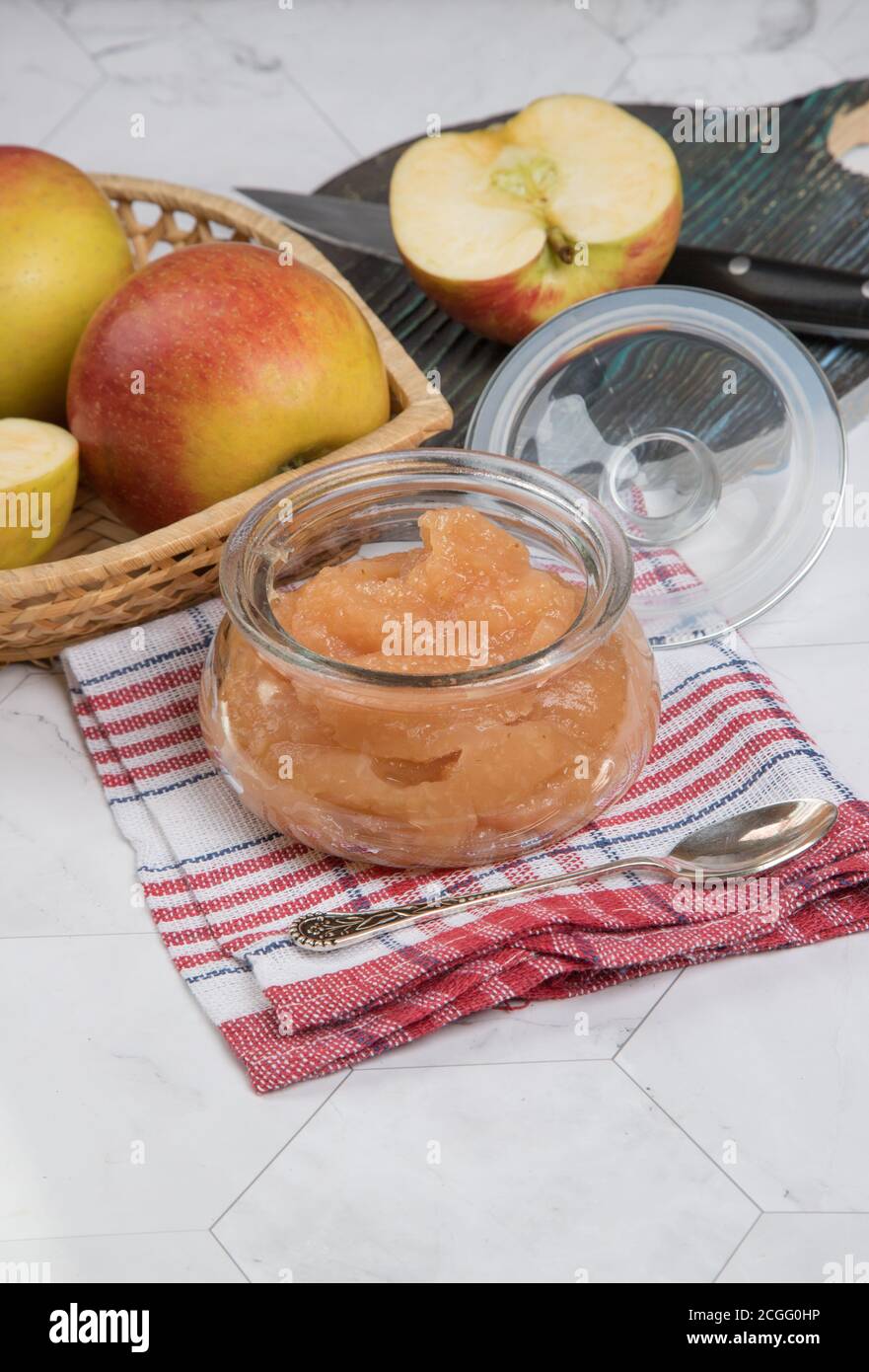 Glas mit Apfelmus und frischen Äpfeln auf einem Teller auf hellem Hintergrund mit karierter Serviette. Vertikale Ausrichtung. Stockfoto