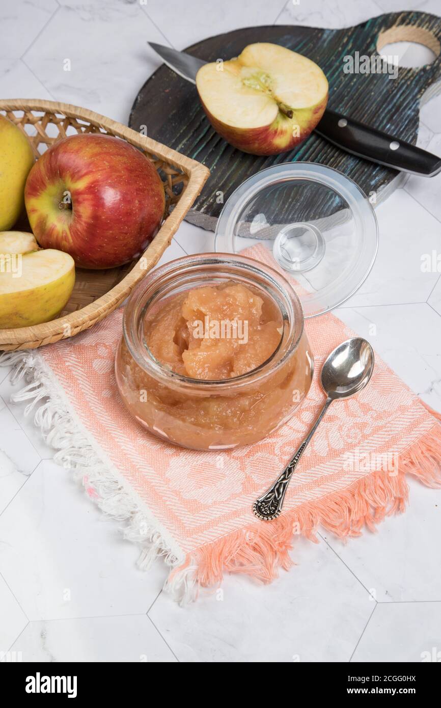 Glas mit Apfelmus und frischen Äpfeln auf einem Teller auf hellem Hintergrund mit rosa Serviette. Vertikale Ausrichtung. Stockfoto